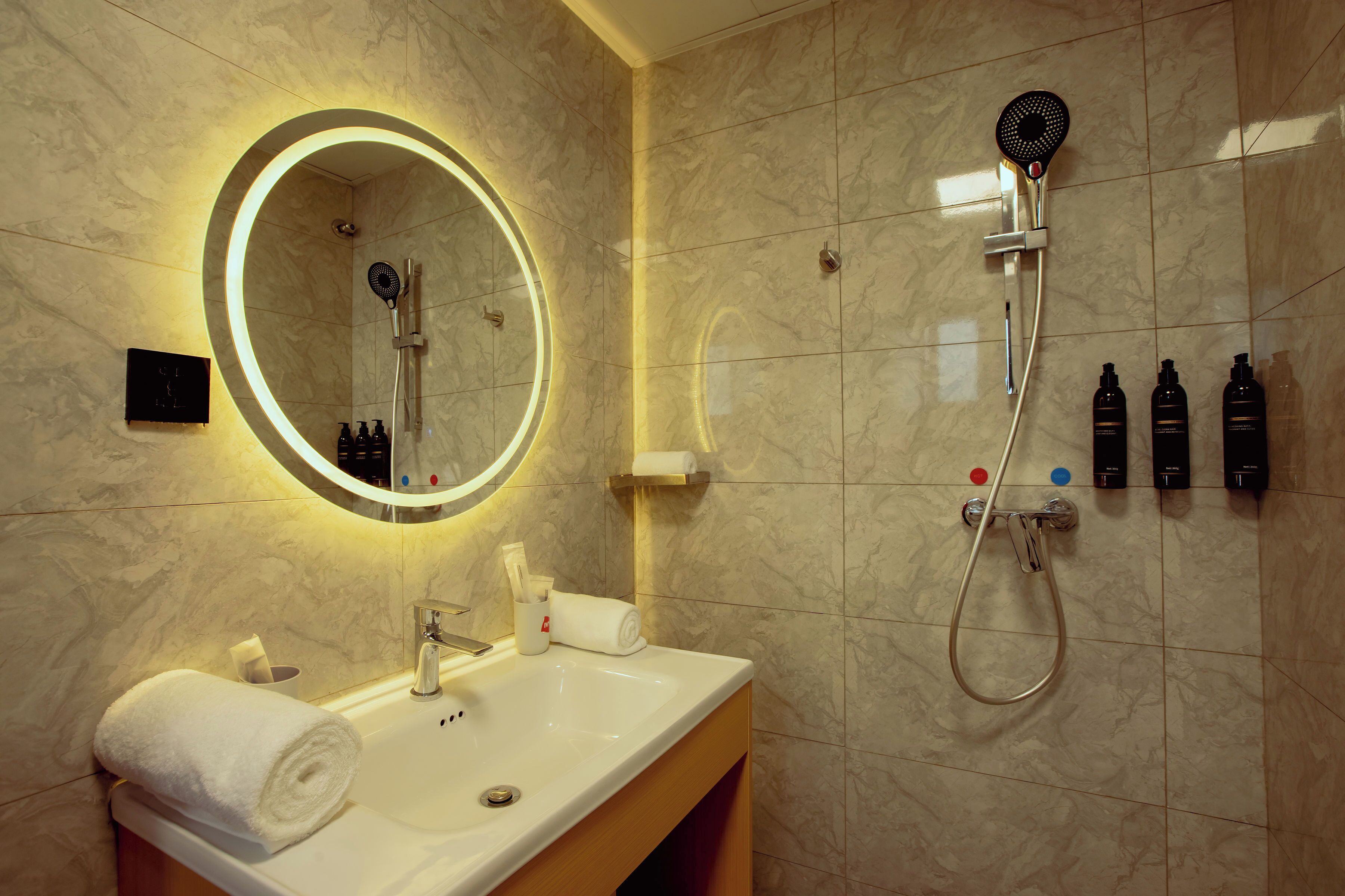 A bathroom with a sink, mirror, shower, and toiletries.