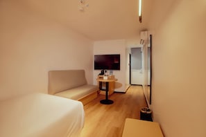 Una habitación de hotel moderna con sofá, una mesita, televisión y puerta de acceso a un baño.