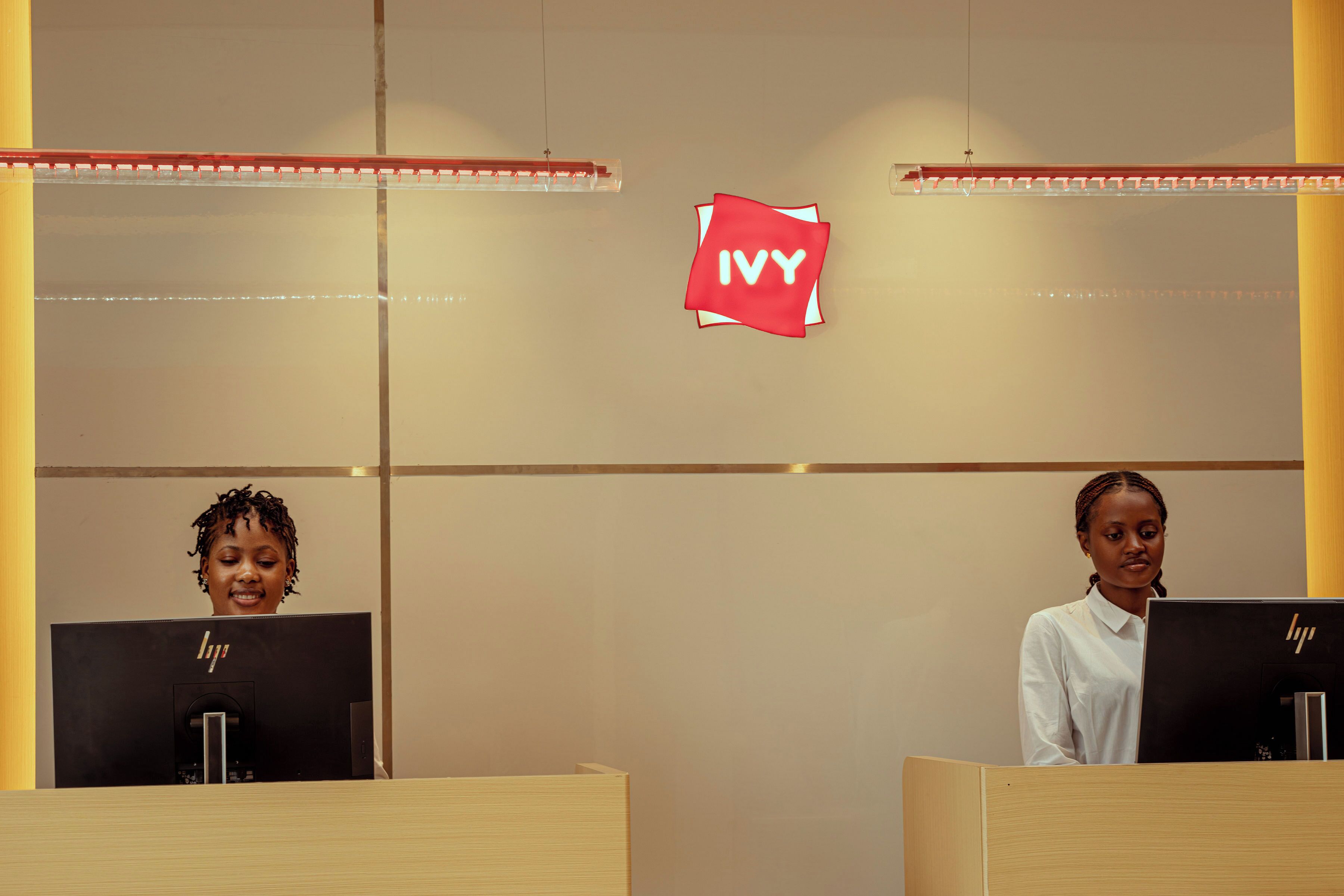 Two receptionists at a desk with a sign that reads 'IVY' above them.