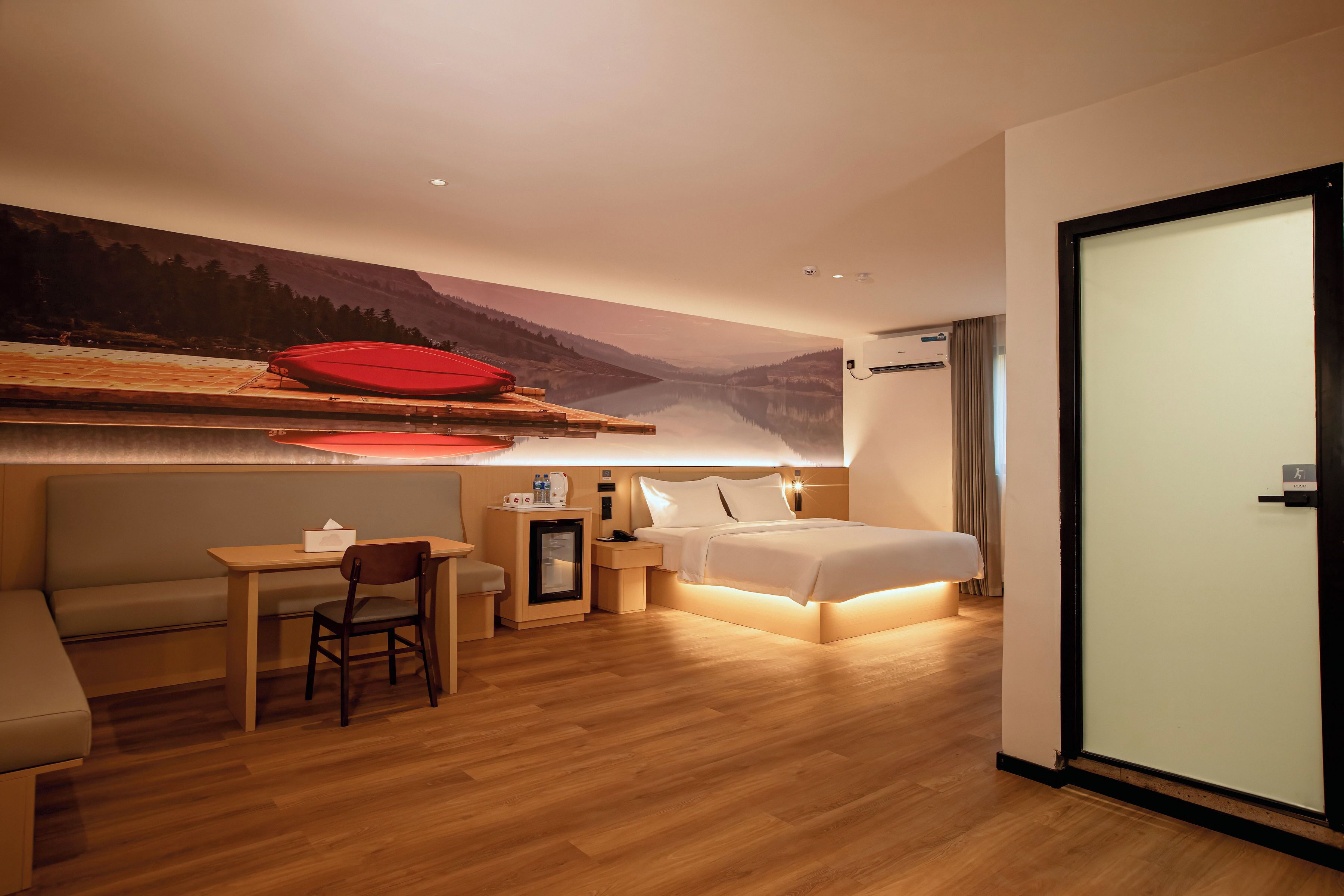 Habitación de hotel con cama, escritorio, silla, refrigerador pequeño y televisor de pared.