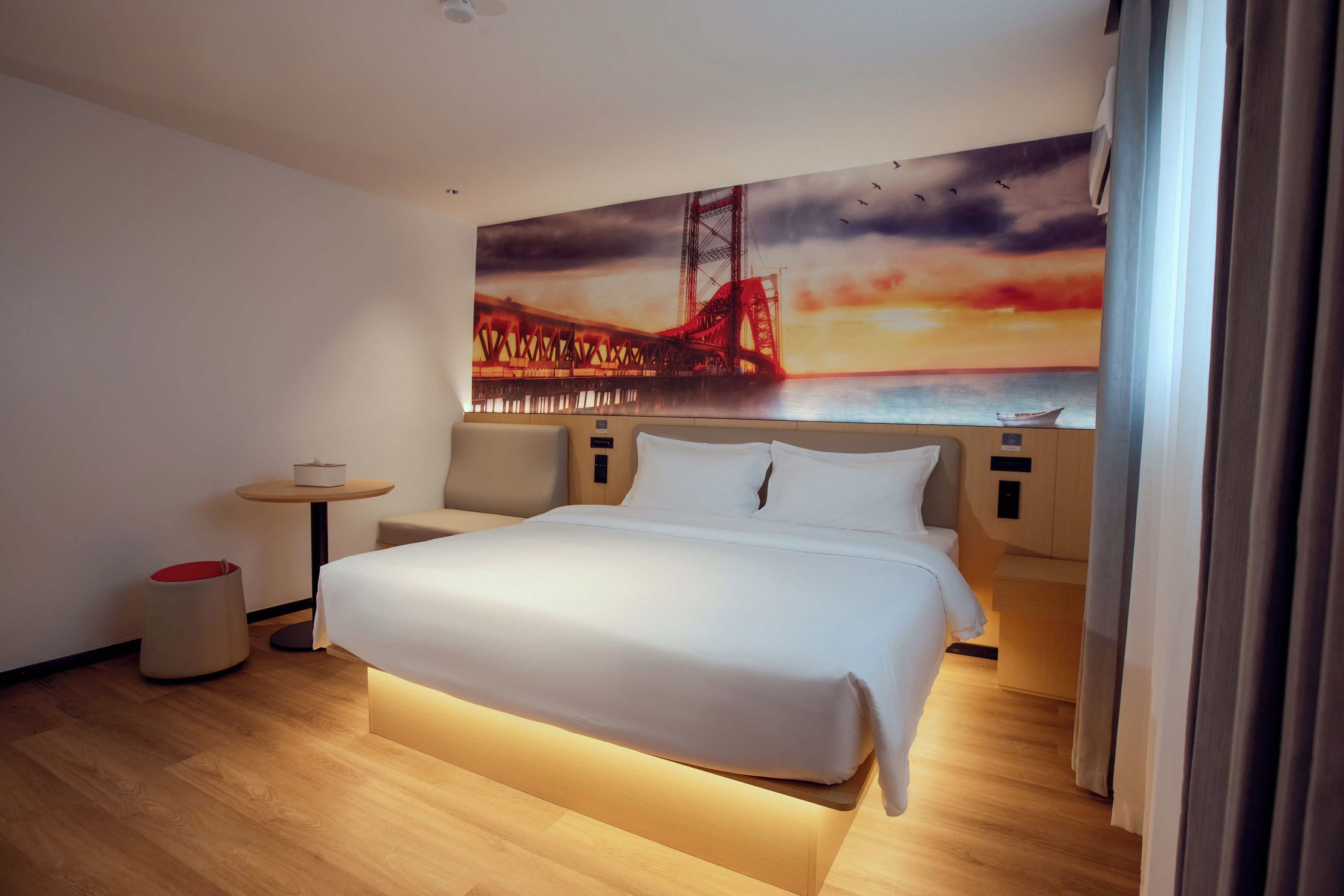 Quarto de hotel com uma cama grande, uma mesa redonda pequena, um sofá e uma pintura de uma ponte.
