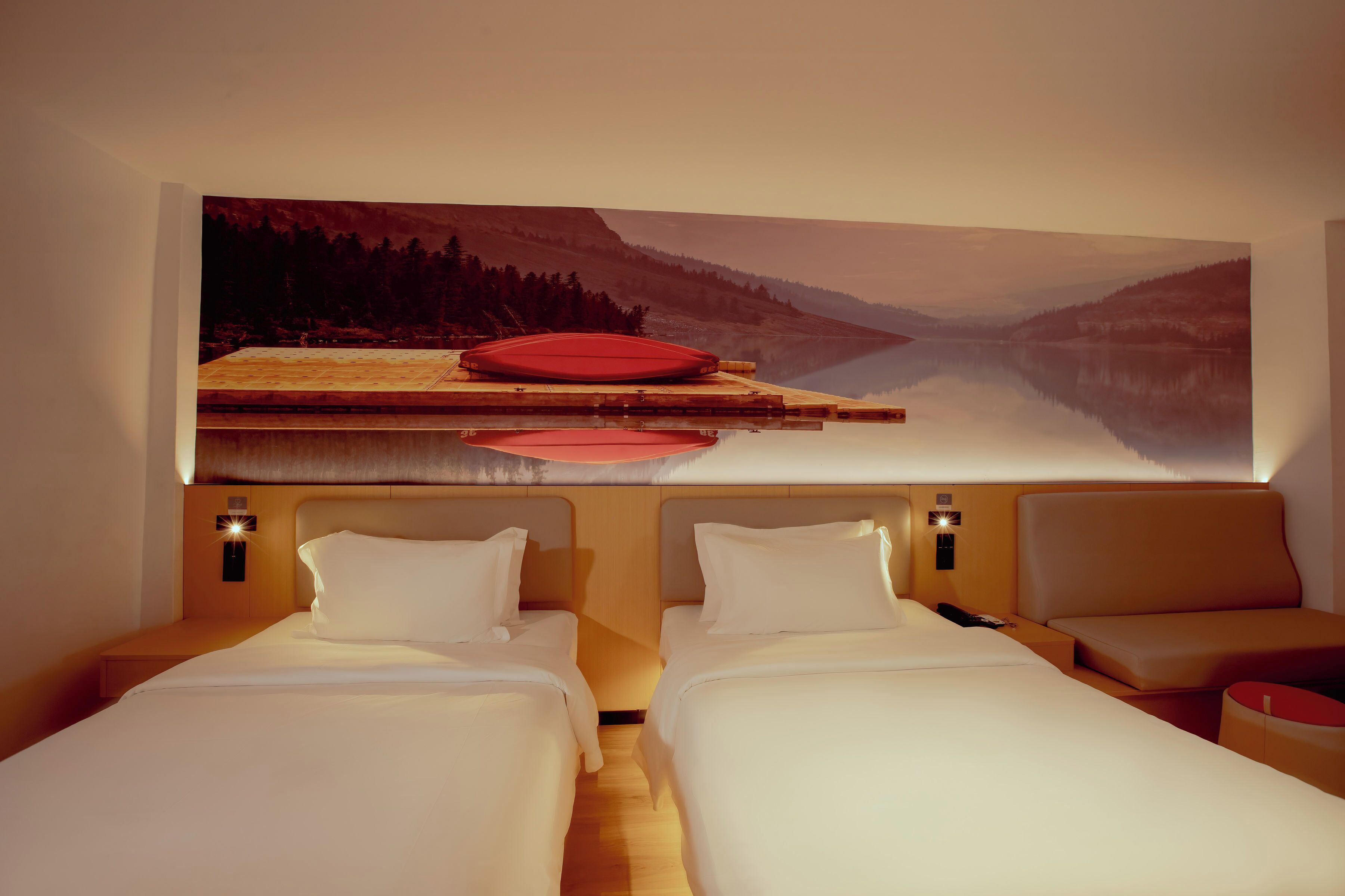 Habitación de hotel con dos camas, un cuadro grande colgado en la pared de un lago y una pala roja en la cabecera.