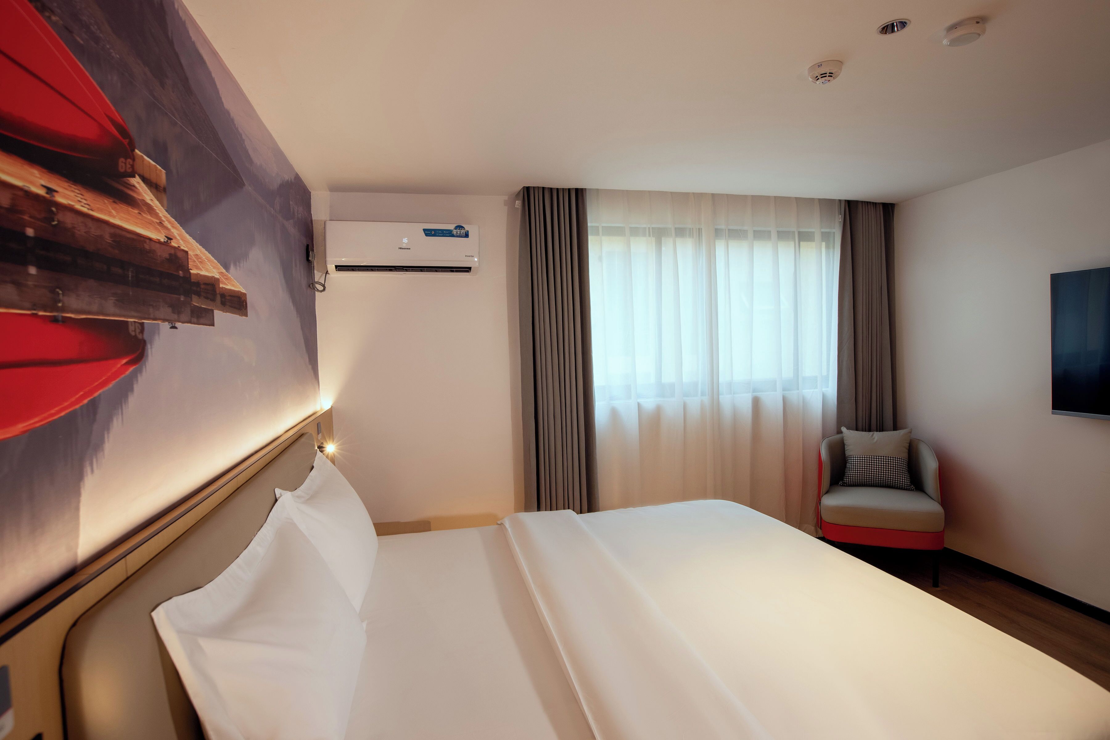Habitació d'hotel amb un llit, una obra d'art penjada, aire condicionat al sostre, una finestra amb cortines i una televisió a la paret.