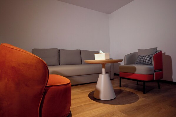 Una sala moderna con un sofá gris, un sillón rojo, una pequeña mesa de madera con una caja de pañuelos y un cojín estampado en una silla roja.