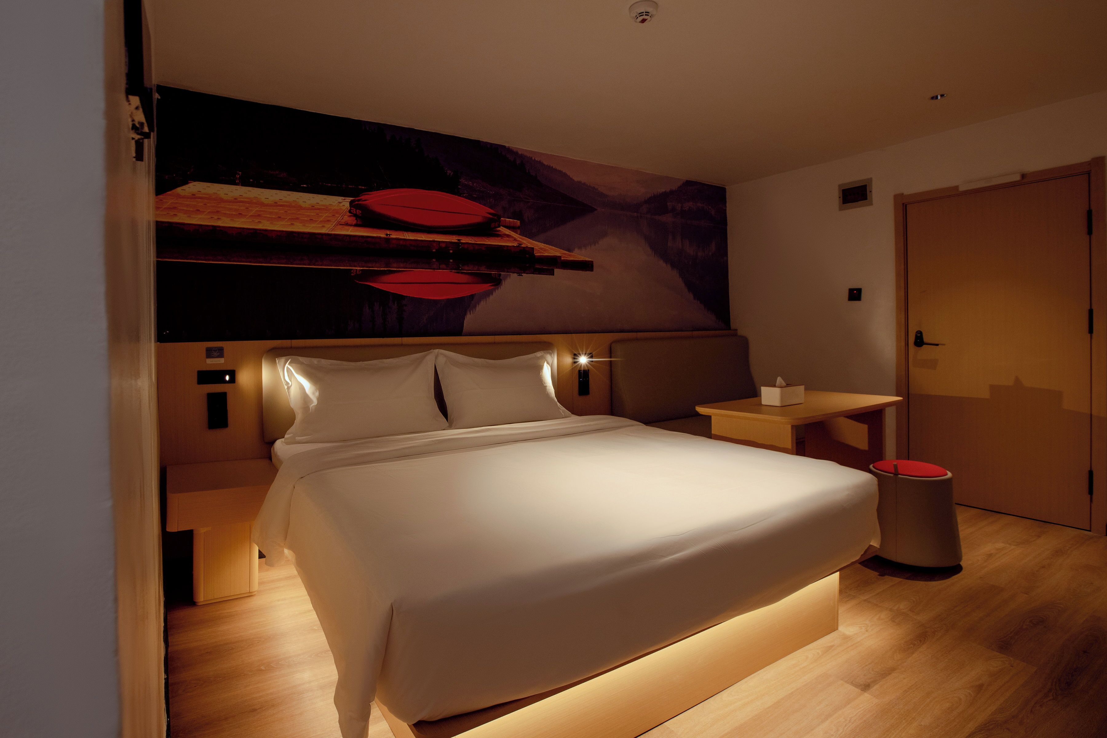 A modern hotel room with a large bed, a desk, and a wall-mounted shelf.