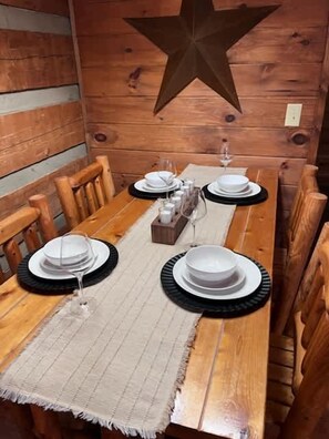 Una mesa de comedor de madera dispuesta con platos, vasos y un centro de mesa.