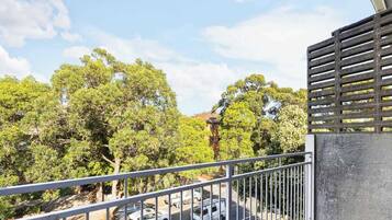 A balcony with a metal railing overlooking a street with cars and trees.