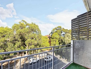 A balcony with a metal railing overlooking a street with cars and trees.