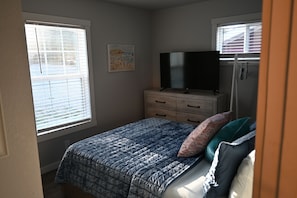 Un dormitorio con cama, cómoda, televisor y ventana con persianas.