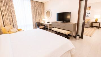 A hotel room with a large bed, a desk with a chair, a television, and a small table with a lamp.