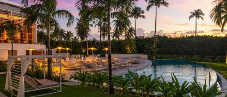 Un resort con piscina, sillones de descanso, palmeras y un edificio moderno.