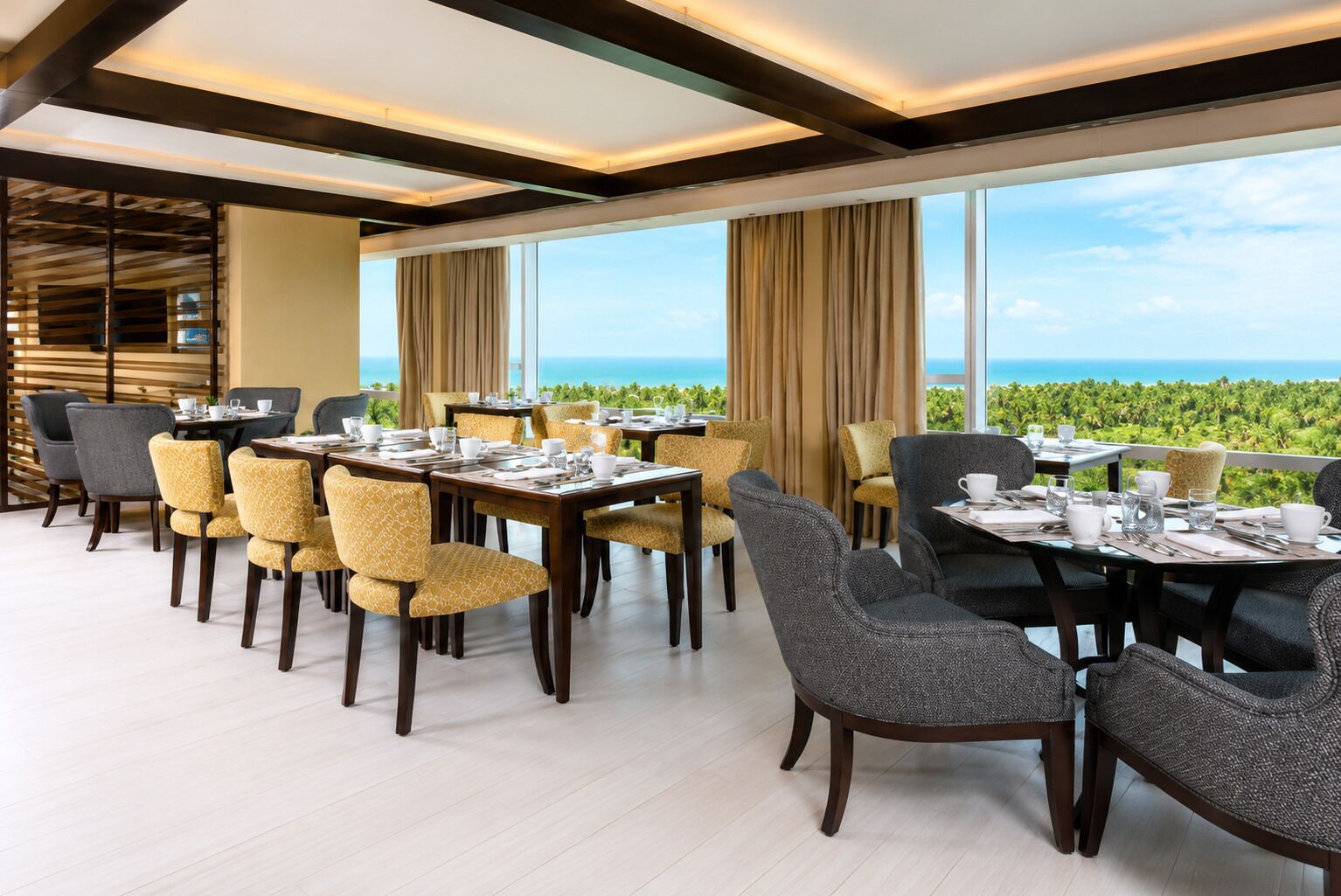 A restaurant with multiple tables and chairs, large windows, and a view of the ocean.