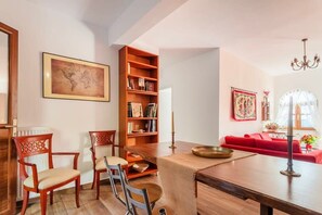 A dining area with a wooden table, chairs, a bookshelf, and a red sofa.