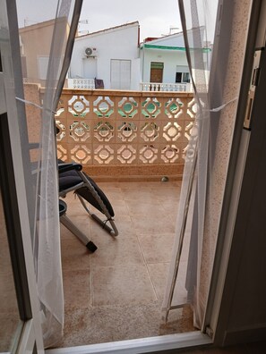 A balcony with a chair, a decorative fence, and a view of neighboring buildings.