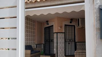 Un espace extérieur aménagé avec un toit, doté d’un mur décoré de motifs, d’un portail noir et d’un canapé en osier.