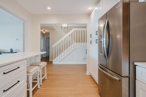 Eine Küche mit einem Edelstahl-Kühlschrank, weißen Schränken, einem Holzboden und einer weißen Treppe, die in einen anderen Raum führt.