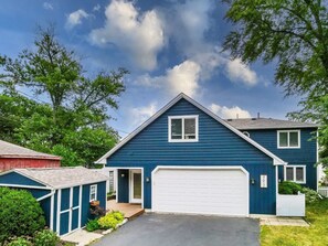 Ein zweistöckiges Haus mit Garage, kleiner Gartenhütte und gepflegtem Rasen.
