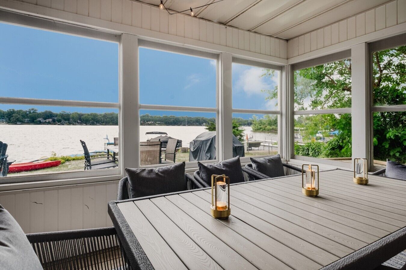 Een overdekt terras met uitzicht op een waterpartij, een tafel met kussens en lantaarnverlichting.