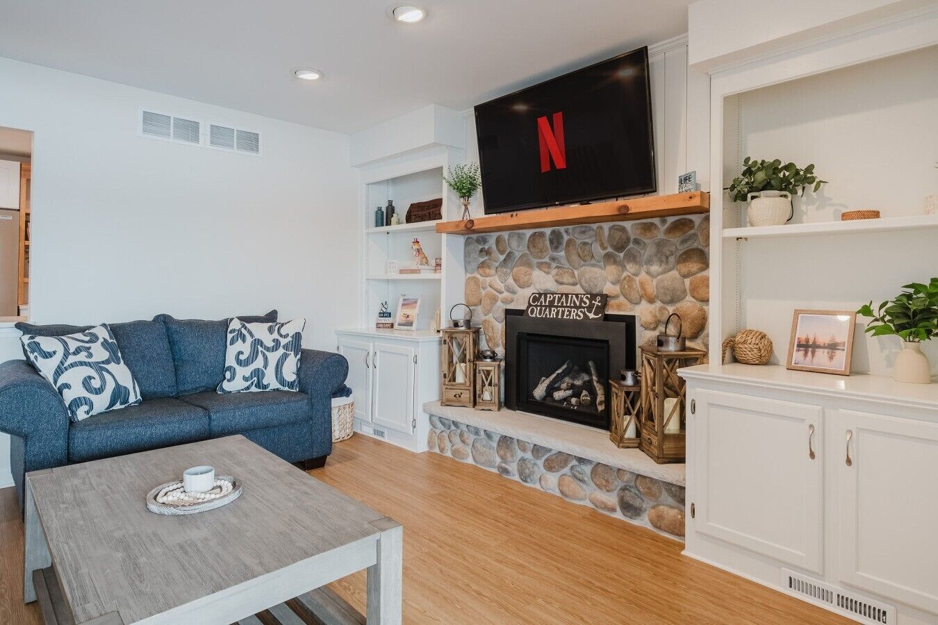 A living room with a stone fireplace, a television mounted above it, a blue sofa, and a coffee table with a tray.