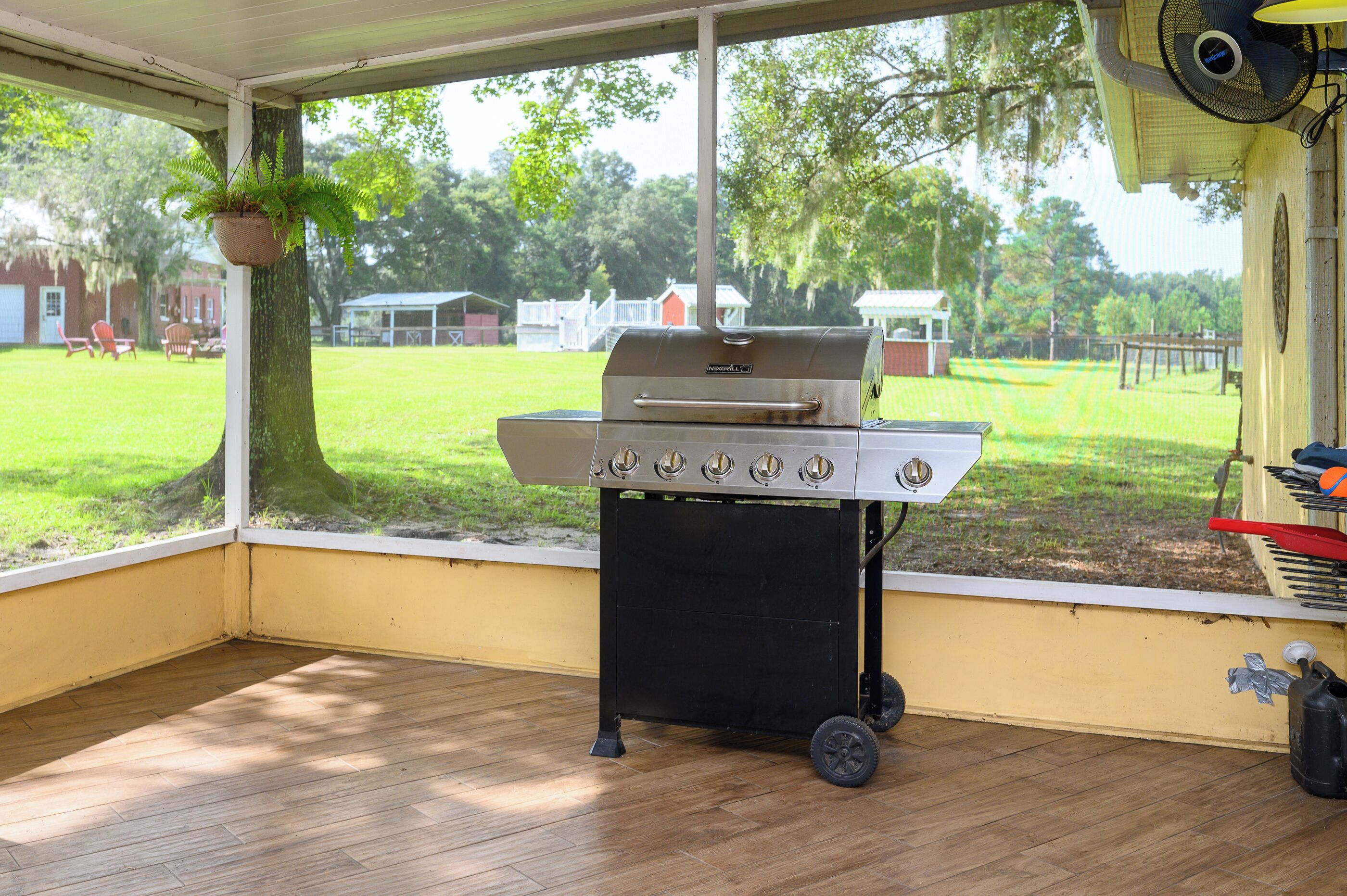 A covered outdoor area with a grill, a hanging plant, and a view of a grassy yard.