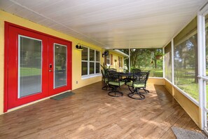 Un patio techado con piso de madera, una puerta roja y una mesa con sillas.