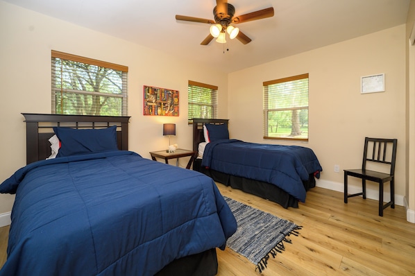 A bedroom with two beds, a ceiling fan, and windows with blinds.