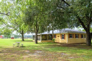 A yellow building with a porch, surrounded by trees and grass.