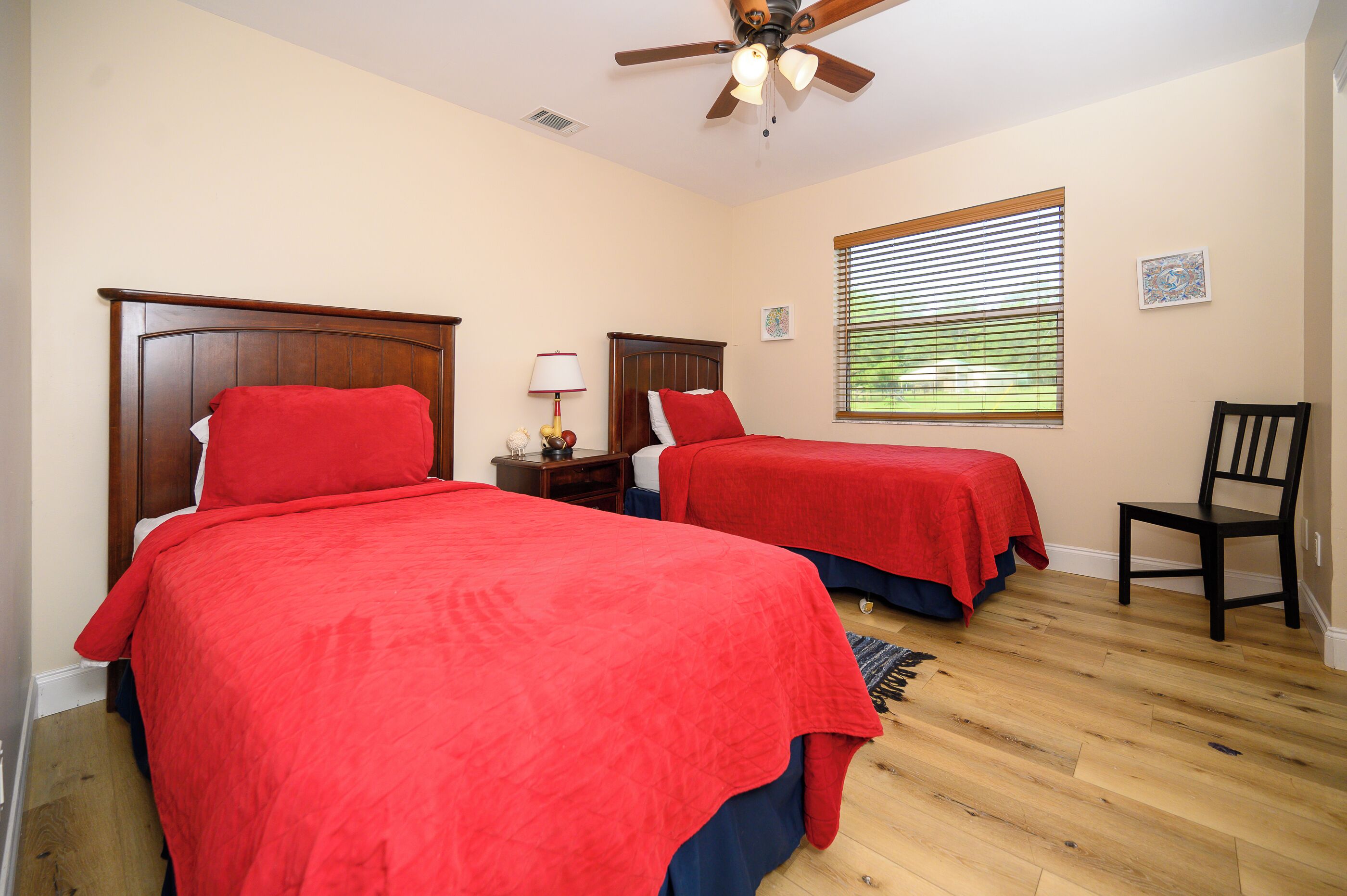 A bedroom with two beds, a ceiling fan, a window with blinds, and a chair.