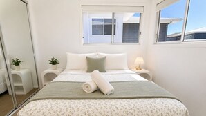 Een slaapkamer met een bed, twee nachtkastjes, een raam en een spiegel.