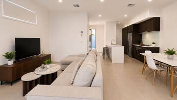 Ein modernes Wohnzimmer mit einer Couch, einem Fernseher und einem Essbereich mit Tisch und Stühlen.