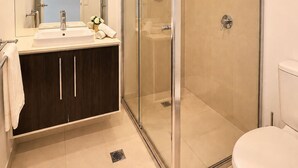 Een moderne badkamer met een glazen douchecabine, een wastafel met spiegel en een toilet.
