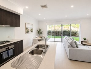 A modern kitchen with a built-in oven, a stainless steel sink, and a dining area with a view of the garden.