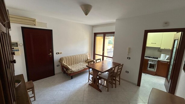 Une pièce comprenant un canapé, une table à manger, des chaises, un coin cuisine et une porte.