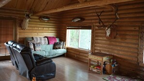 A log cabin interior with a leather sofa, a small table with books, and a deer skull on the wall. - Cozy Riverside Cabin (Riverside)