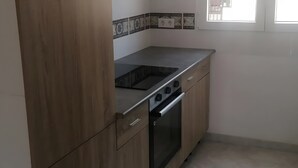 A kitchen with wooden cabinets, a black stove, and a window above the sink. - Holiday Home 'Lustigmann 2' with Private Terrace, Wi-Fi and Air Conditioning (San Fulgencio)