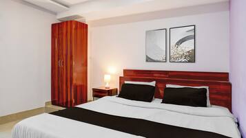 A bedroom with a bed, a nightstand, a lamp, a wardrobe, and two wall art pieces.