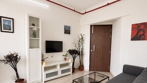 En moderne stue med en sofa, et fladskærms-tv, et sofabord i glas og en reol.