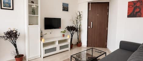Una sala de estar moderna con un sofá, un televisor de pantalla plana, una mesa de centro de vidrio y una estantería.