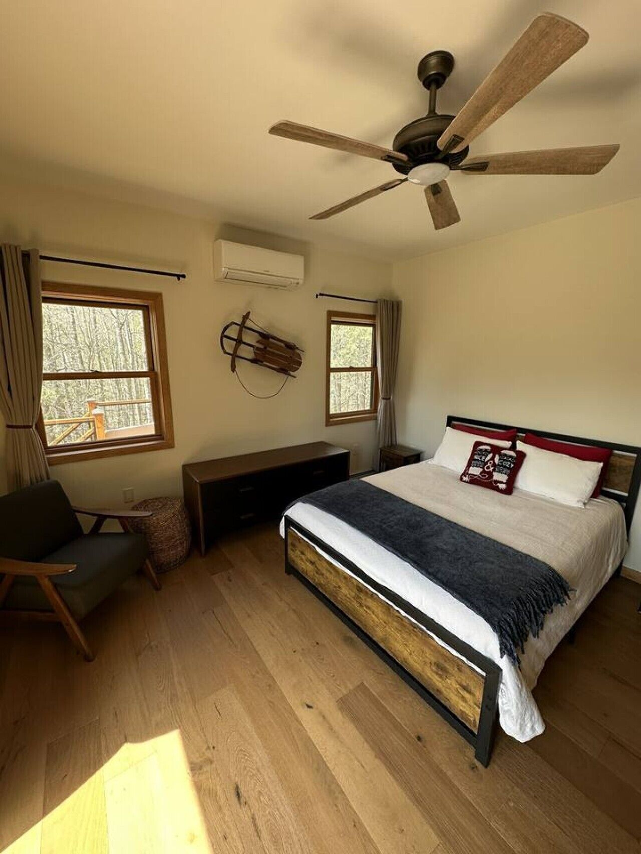A bedroom with a bed, a desk, a chair, a ceiling fan, and two windows.