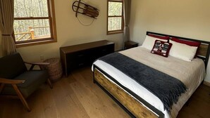 A bedroom with a bed, a desk, a chair, a ceiling fan, and two windows.
