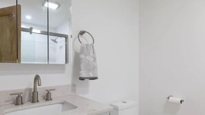 Et badeværelse med vask, spejl, håndklædestang, toilet og toiletpapir.