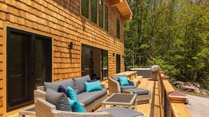 A wooden cabin with a deck furnished with outdoor seating and a hot tub.