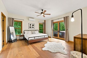 A bedroom with a bed, a ceiling fan, a large window, and a view of greenery outside.