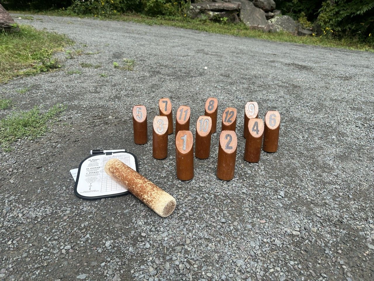 A set of numbered wooden blocks on a gravel surface with a chalkboard and a piece of chalk.
