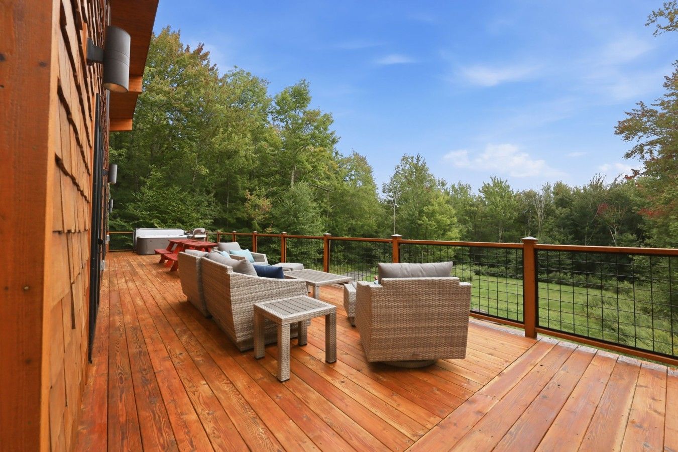 En træterrasse med udendørs møbler, et spabad og udsigt til en skov.