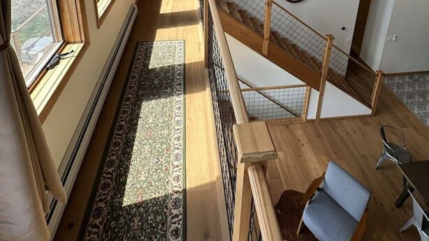 A spacious interior with a high ceiling, wooden beams, a staircase, and a view of the outdoors.
