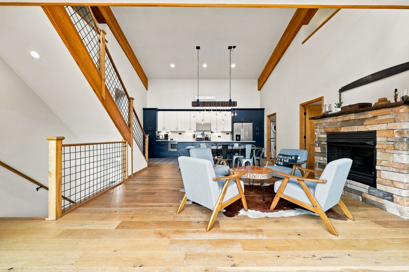 Un vaste espace de vie doté d’un haut plafond, une table à manger avec des chaises, une cheminée et une cuisine à l’arrière-plan.