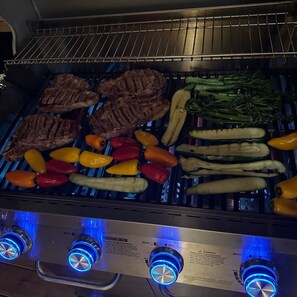 Uma churrasqueira com diversos tipos de carne e legumes sendo preparados.