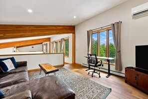 A modern living room with a sofa, a small table, a TV, and a desk with a chair. - Catskills Escape w/ Hot Tub & Fireplace (Jewett)
