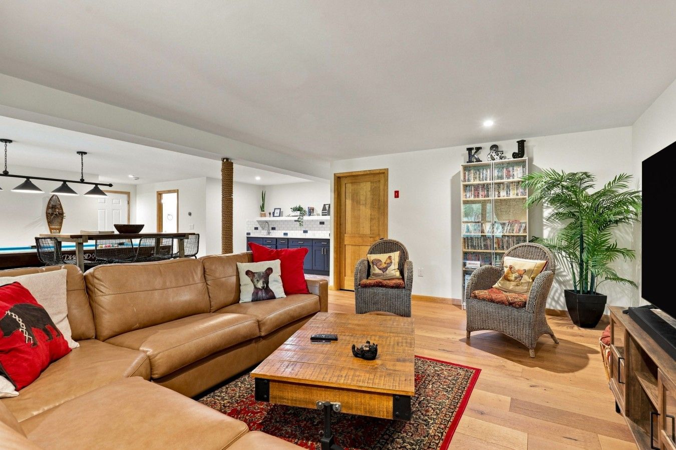 A modern living room with a leather sofa, two wicker chairs, a coffee table, and a bookshelf.